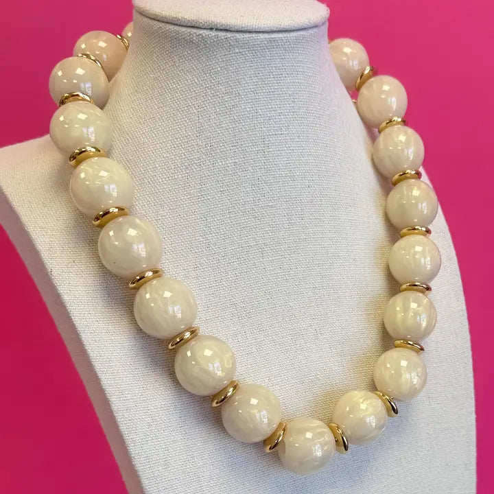 Ivory marbled statement bead necklace with gold-tone spacer accents, displayed on a jewelry bust.