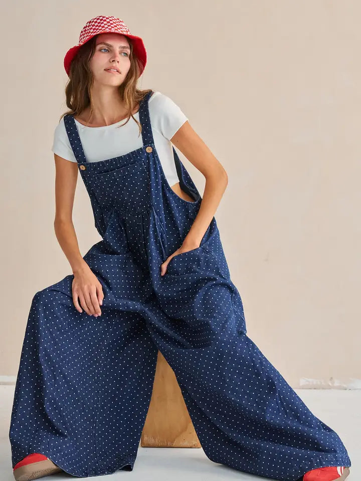 Navy polka dot wide-leg overall jumpsuit, seated pose showing wide leg silhouette