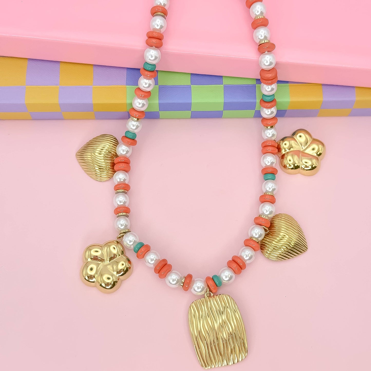 Necklace with gold pendants and coral beads on a colorful checkered background
