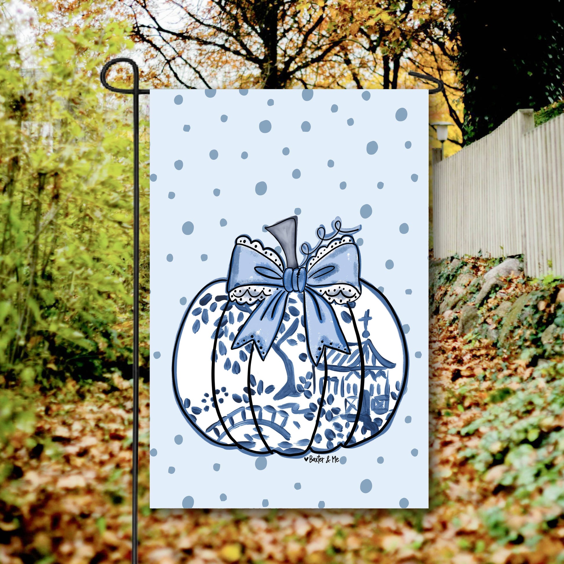 Decorative garden flag with a blue bow and pumpkin design on a white background, standing outdoors.