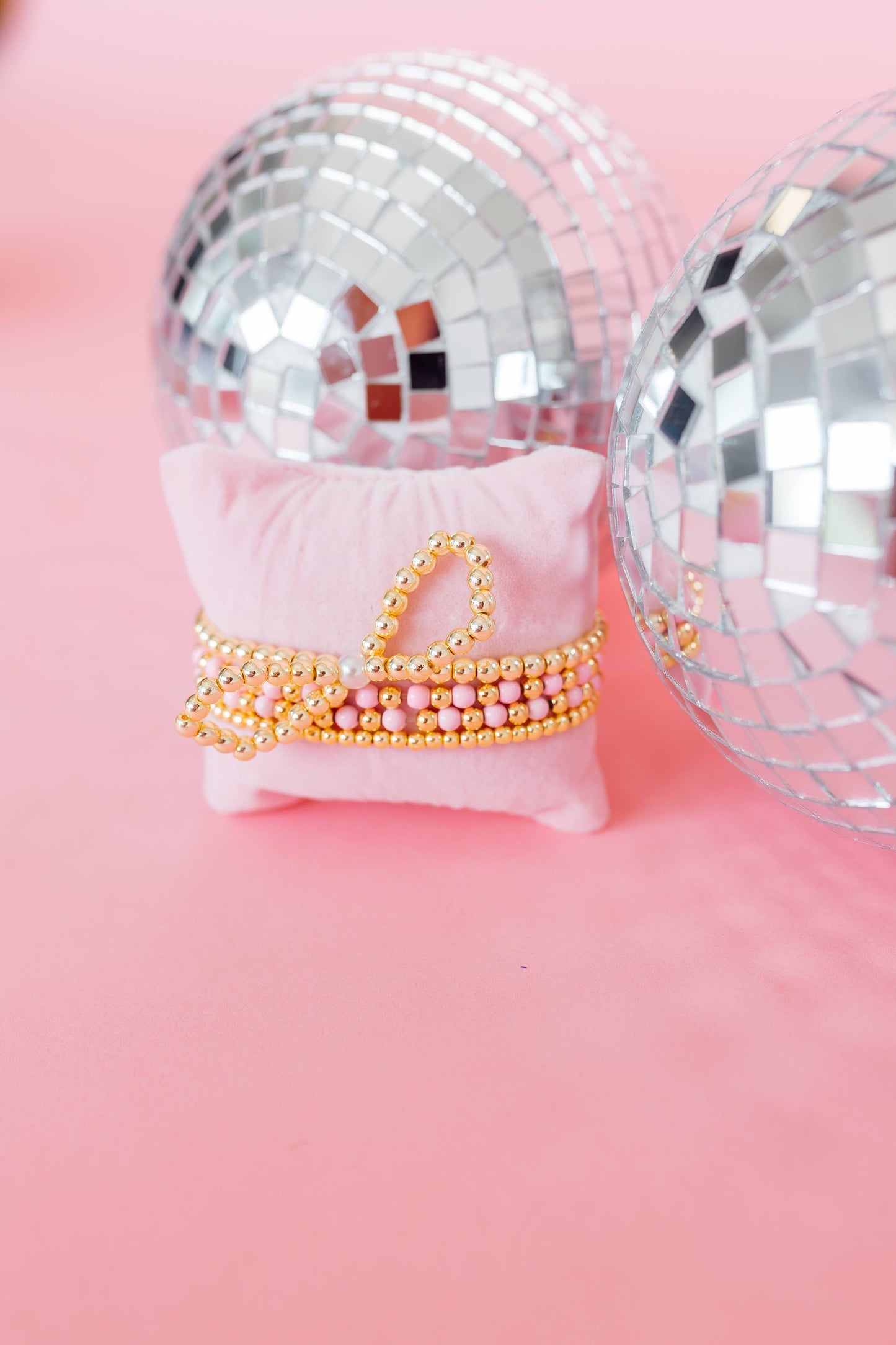 Decorative crown with gold and pink accents on a pink pillow, surrounded by disco balls on a pink background