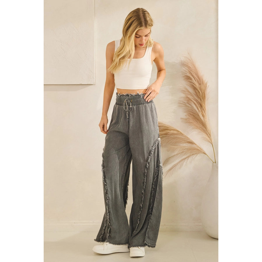 Woman wearing a white tank top and gray wide-leg pants in a minimalistic setting.