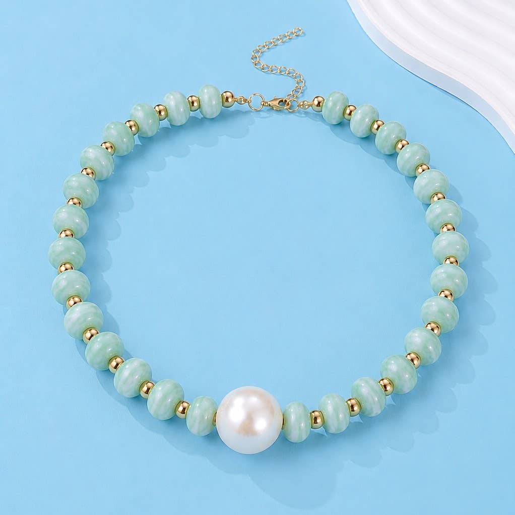 A beaded necklace featuring light green stone beads, small gold spacer beads, and a large white pearl at the front, displayed on a light blue background.