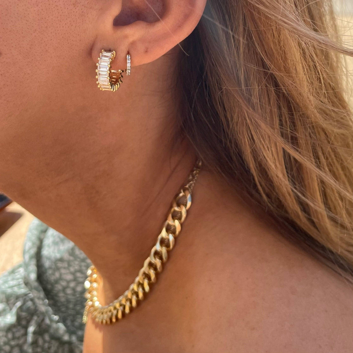 Close-up of a person wearing gold hoop earrings and a gold chain necklace.