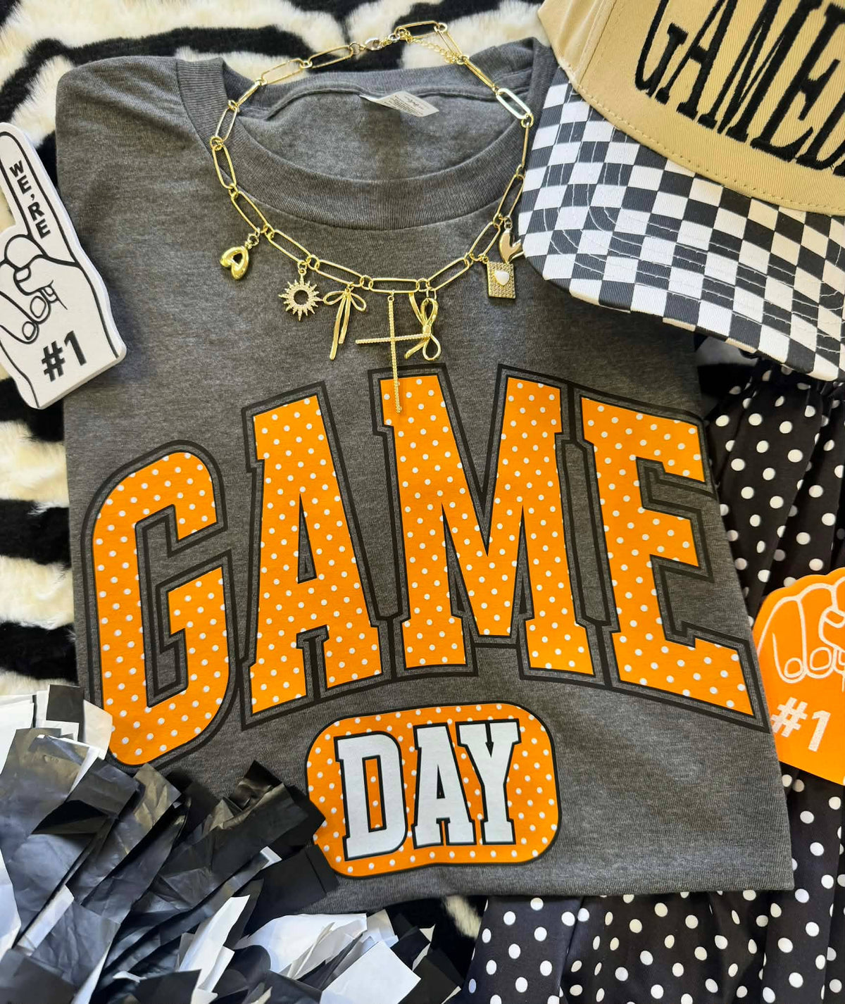 Gray t-shirt with 'GAME DAY' text in orange and white, surrounded by accessories on a patterned surface.