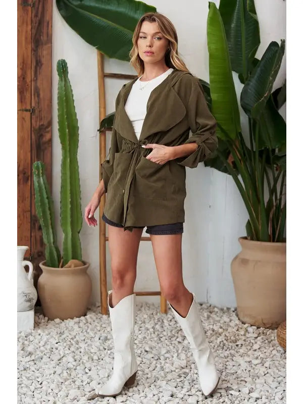 Olive lightweight hooded jacket, front view with waist tie bow, open over white top and black shorts