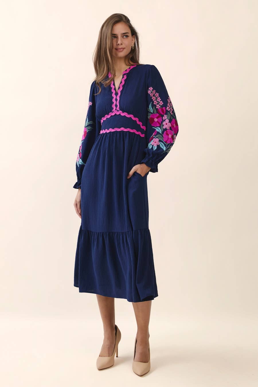 Woman wearing a blue dress with pink floral embroidery on a beige background