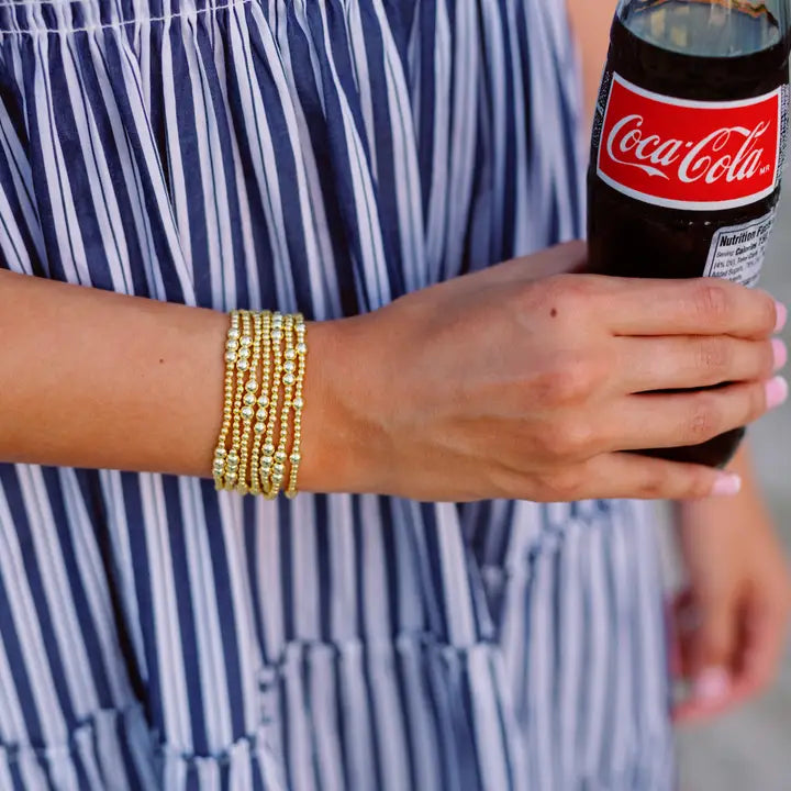 Person holding a Coca-Cola can with a blue and white striped dress and gold bracelet.