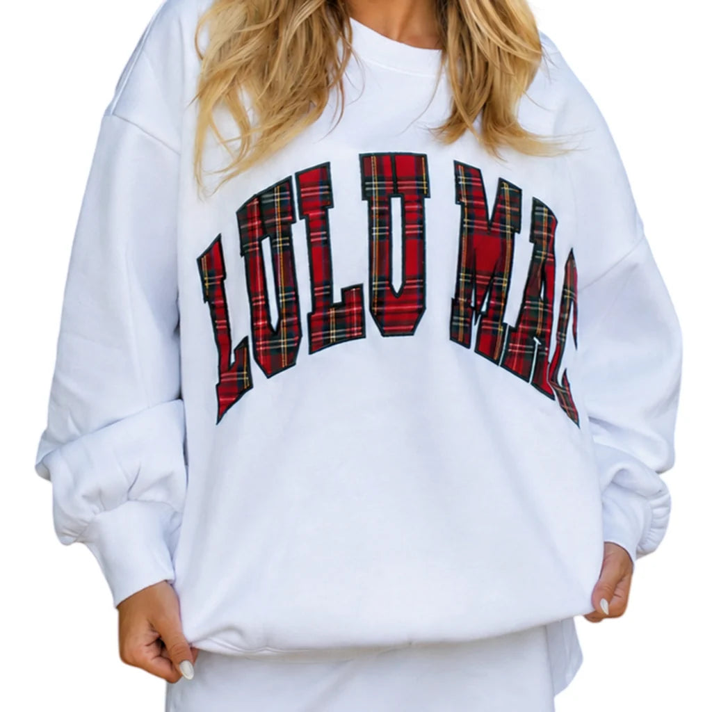 Woman wearing a white Lulu Mac oversized crewneck sweatshirt with bold red and black plaid lettering, styled with black leggings.