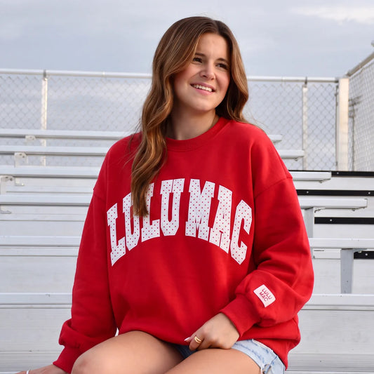 a model wearing a red lulu mac sweatshirt with white lulu mac in lettering and red polka dots
