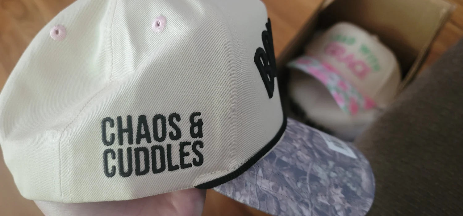 Close up of Boy Mom Chaos and Cuddles embroidery on cream trucker hat with black rope trim and acid wash brim