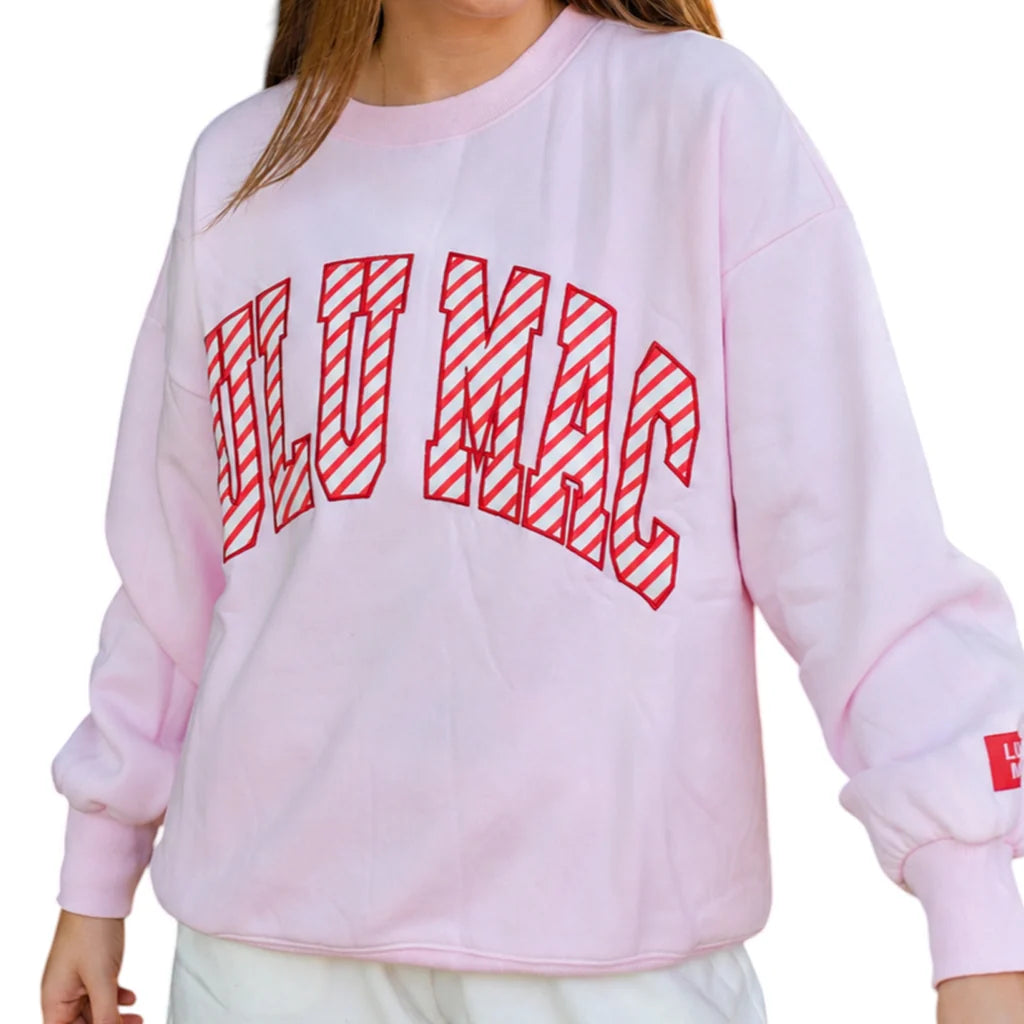 A person wearing a light pink crewneck sweatshirt with 'LULU MAC' printed across the chest in red outlined letters filled with diagonal stripes. The photo is cropped from the neck down against a plain white background.